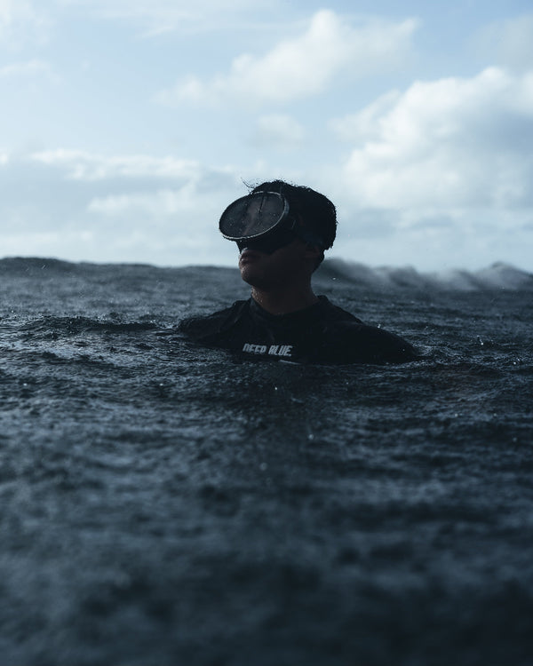 Person wearing a wetsuit and diving mask in the ocean with a cloudy sky.