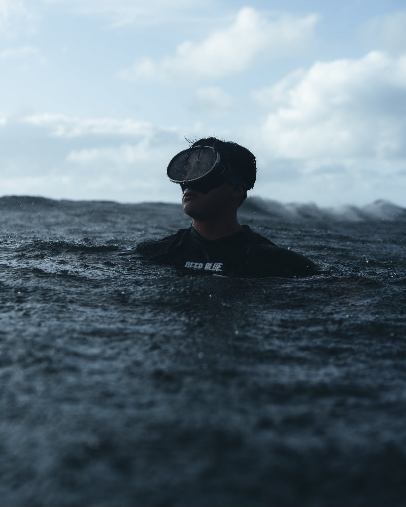Person wearing a wetsuit and diving mask in the ocean with a cloudy sky.