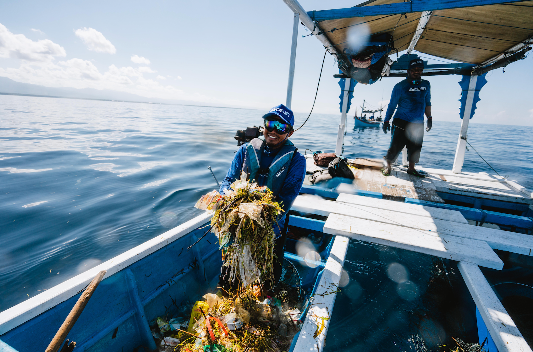 Two people on a boat collecting marine debris in the ocean.